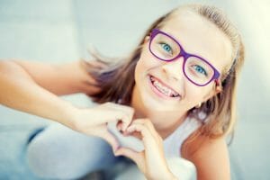 girl with purple glasses and braces making heart with hands